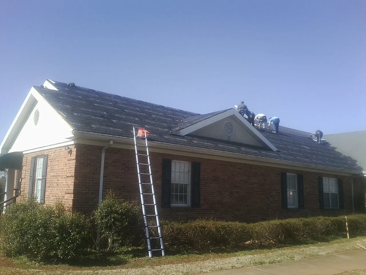Crew tearing shingles off a brick ranch roof with a ladder set — Metal Roof Repair work by our crew in Pacific City