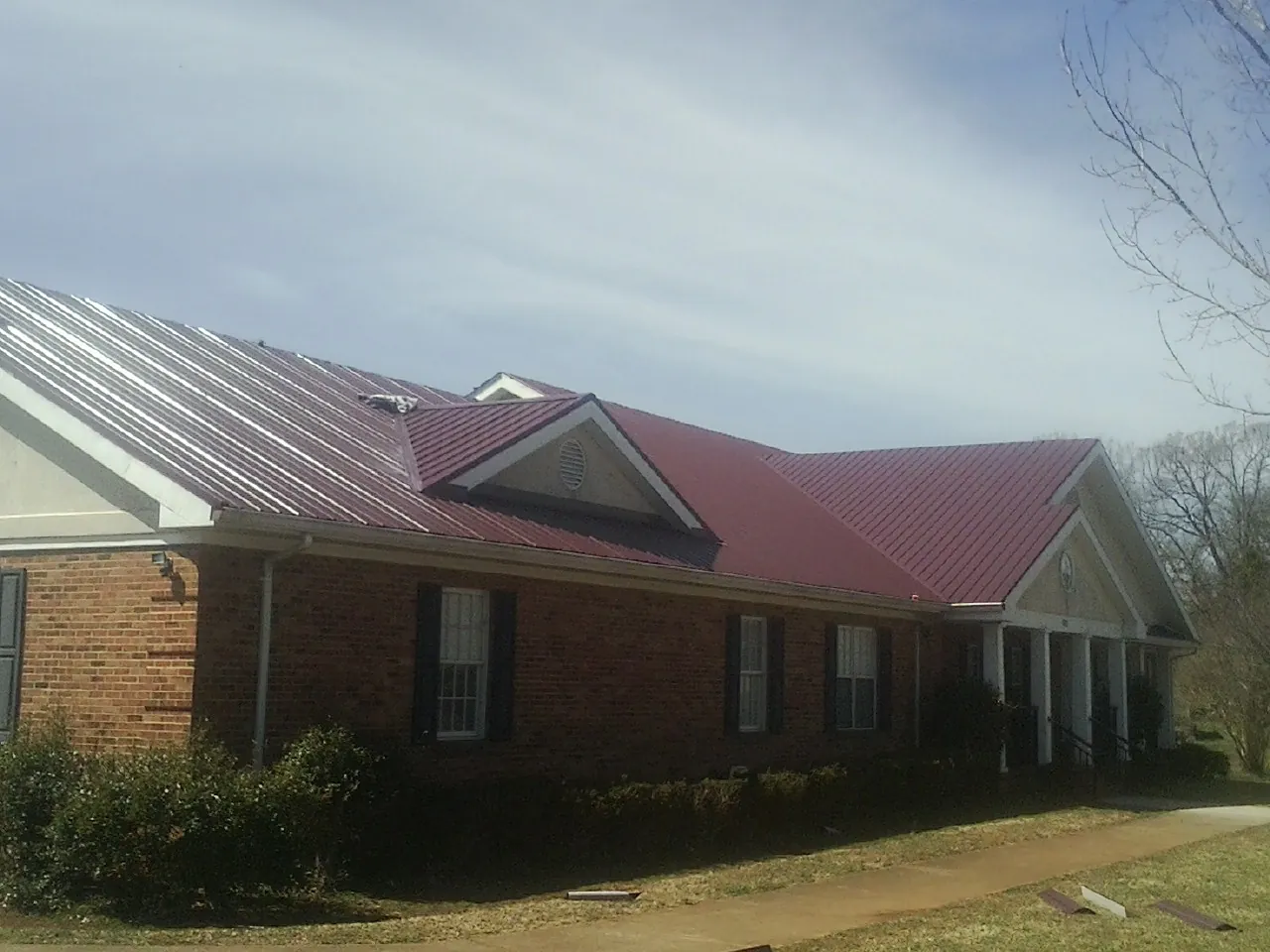Red metal roof with gabled entries on a long brick building, from a Hail Damage Roof Repair job in Pacific City