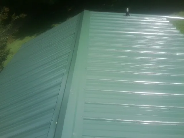 New green metal panels meeting at the ridge of a roof — Flat Roof Repair work by our crew in Pacific City