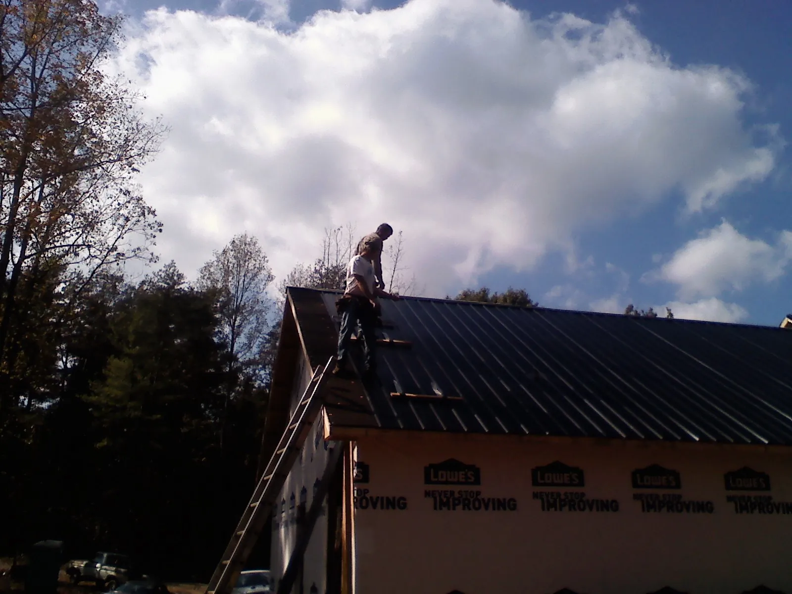 Roofer fastening dark metal panels high against a cloudy sky, from a Roof Inspection job in Pacific City