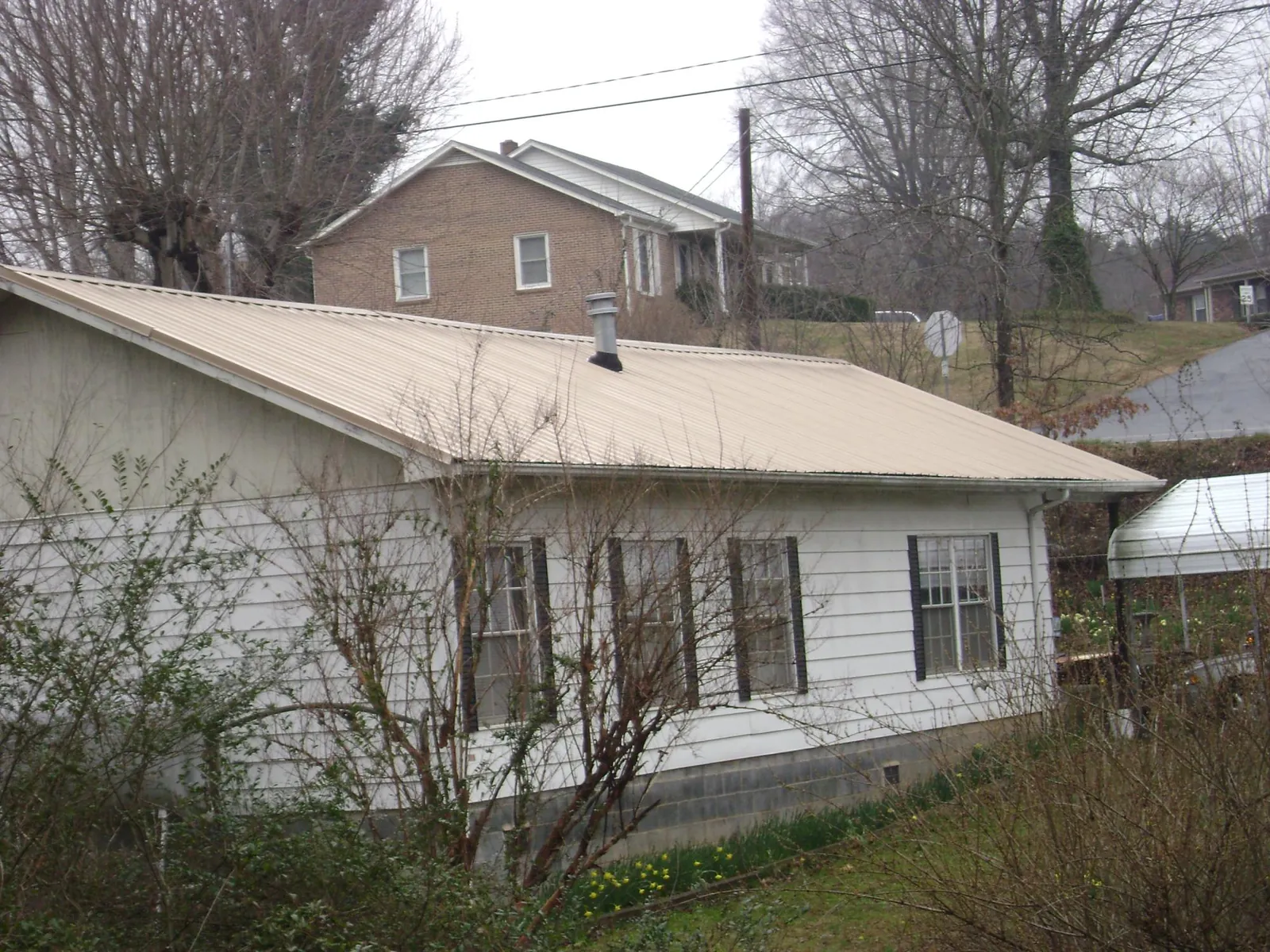Tan metal roof on a white sided house set into a hillside — Commercial Roofing by Roofing Brothers in Pacific City
